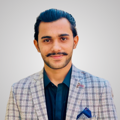 A young man in a checked blazer and dark shirt smiling.